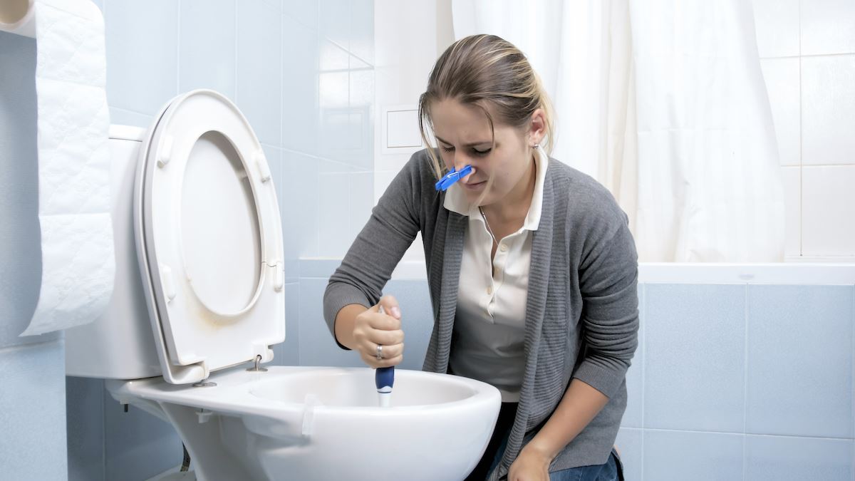 https://www.tubshroom.com/cdn/shop/articles/Woman-unclogging-a-toilet-while-wearing-a-nose-clip_1200x675.jpg?v=1627446032