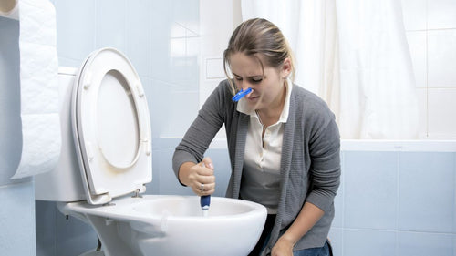 https://www.tubshroom.com/cdn/shop/articles/Woman-unclogging-a-toilet-while-wearing-a-nose-clip_500x.jpg?v=1627446032